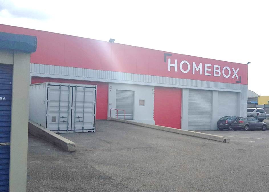Façade rouge avec enseigne HOMEBOX, rideaux métalliques et conteneur de stockage, HOMEBOX Lyon Sud, 53 boulevard Marcel Sembat à Vénissieux