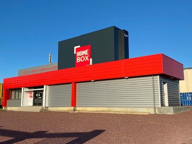 Red and grey facade with HOMEBOX sign and rolling shutters under blue sky at HOMEBOX Saint-Lô, 377 Rue Léon Jouhaux, Saint-Lô