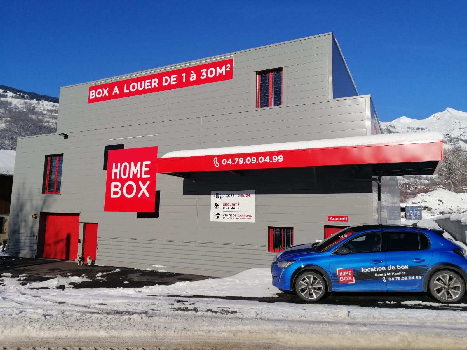 Vue extérieure du centre HOMEBOX Bourg-Saint-Maurice, 220 rue des Colombières, avec bâtiment gris et rouge et voiture stationnée.