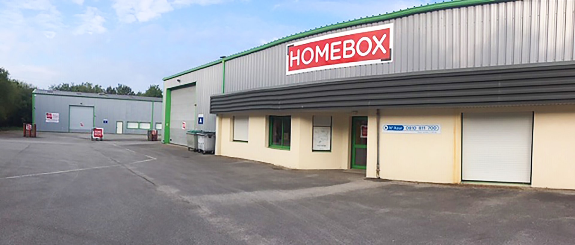 Beige building with red logo and green trim above empty parking lot at HOMEBOX Auray, ZA de Kerstran, Brech