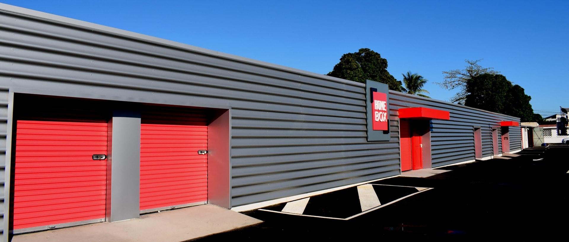 Grey corrugated storage building with red roll-up doors and HOMEBOX sign under blue sky at HOMEBOX La Réunion, 40 rue Mahatma Gandhi, La Possession