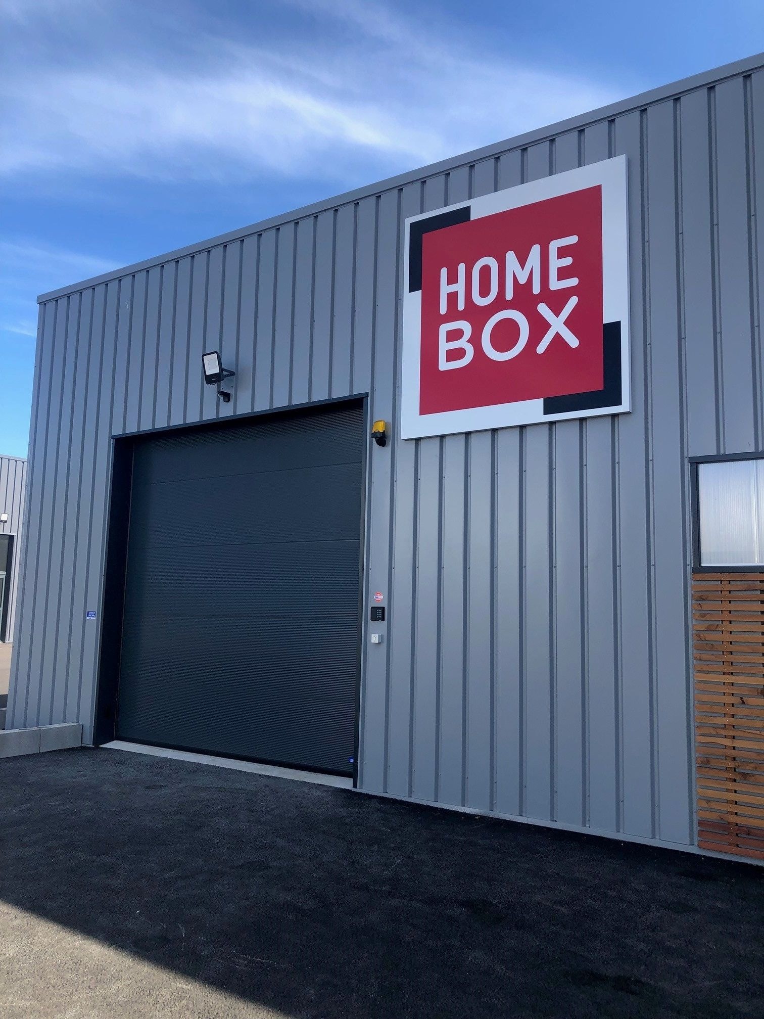 Grey metal facade with large red logo and dark garage door at HOMEBOX Lorient Quéven, 7 Rue André Ampère, Quéven