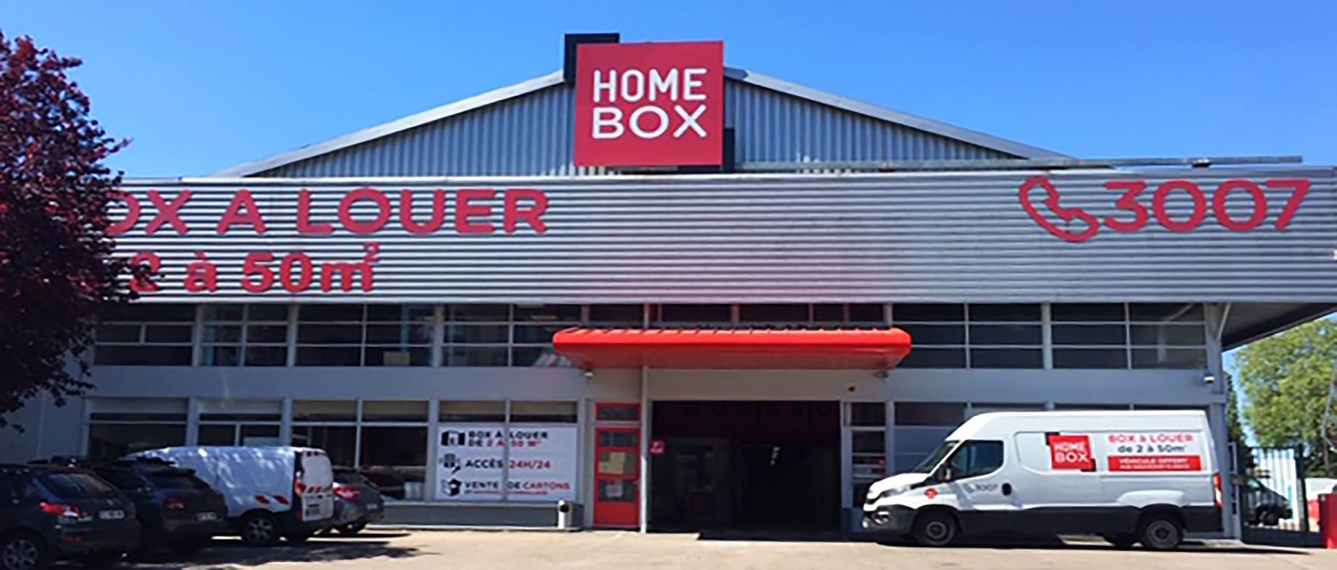 Grey and red building facade with HOMEBOX sign, Box à Louer lettering and parked vehicles at HOMEBOX Rouen, 20-24 rue Adrienne Bolland, Petit Quevilly