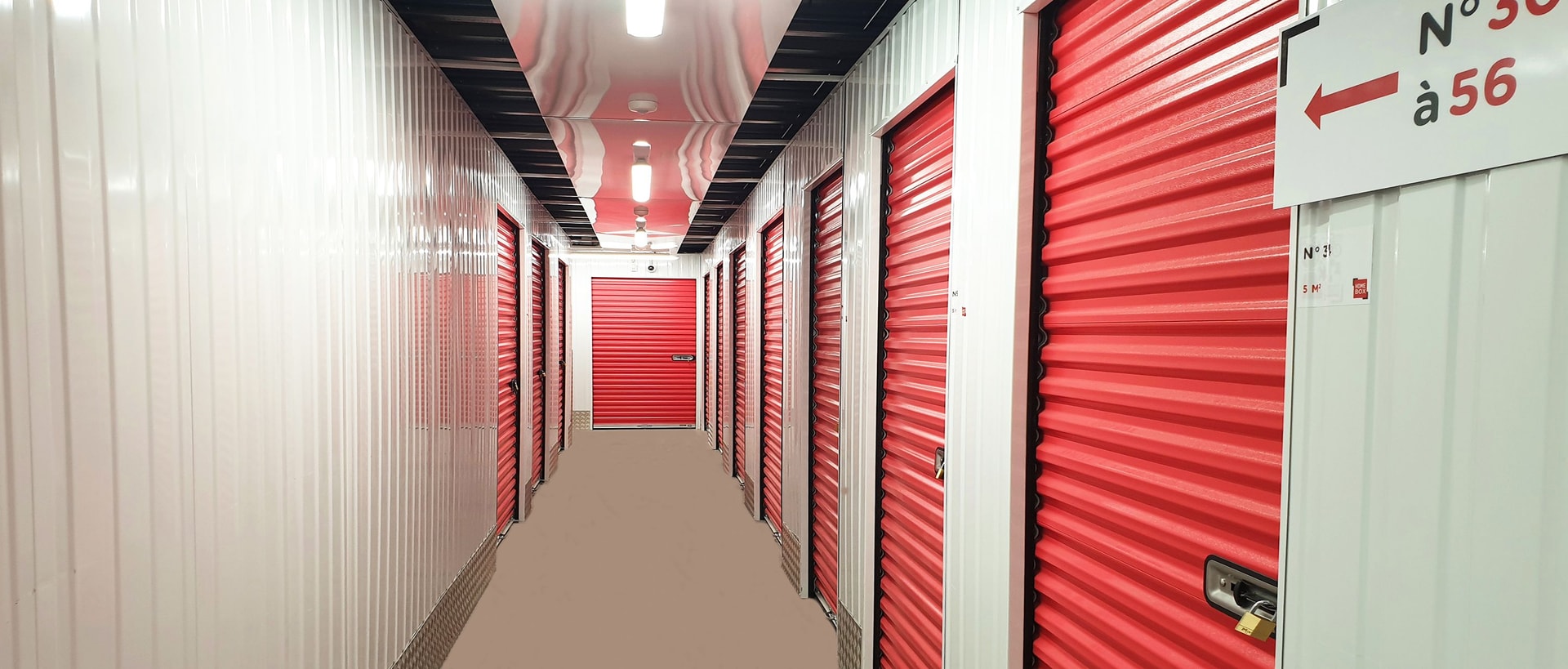 Bright corridor lined with red roll-up storage unit doors at HOMEBOX Cébazat