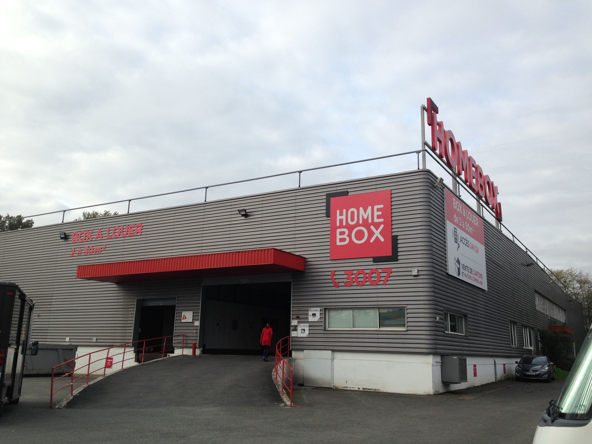 Grey corrugated building with red awning and illuminated HOMEBOX rooftop sign at HOMEBOX Bordeaux Bruges, 1 rue de L'Hermite, Bruges
