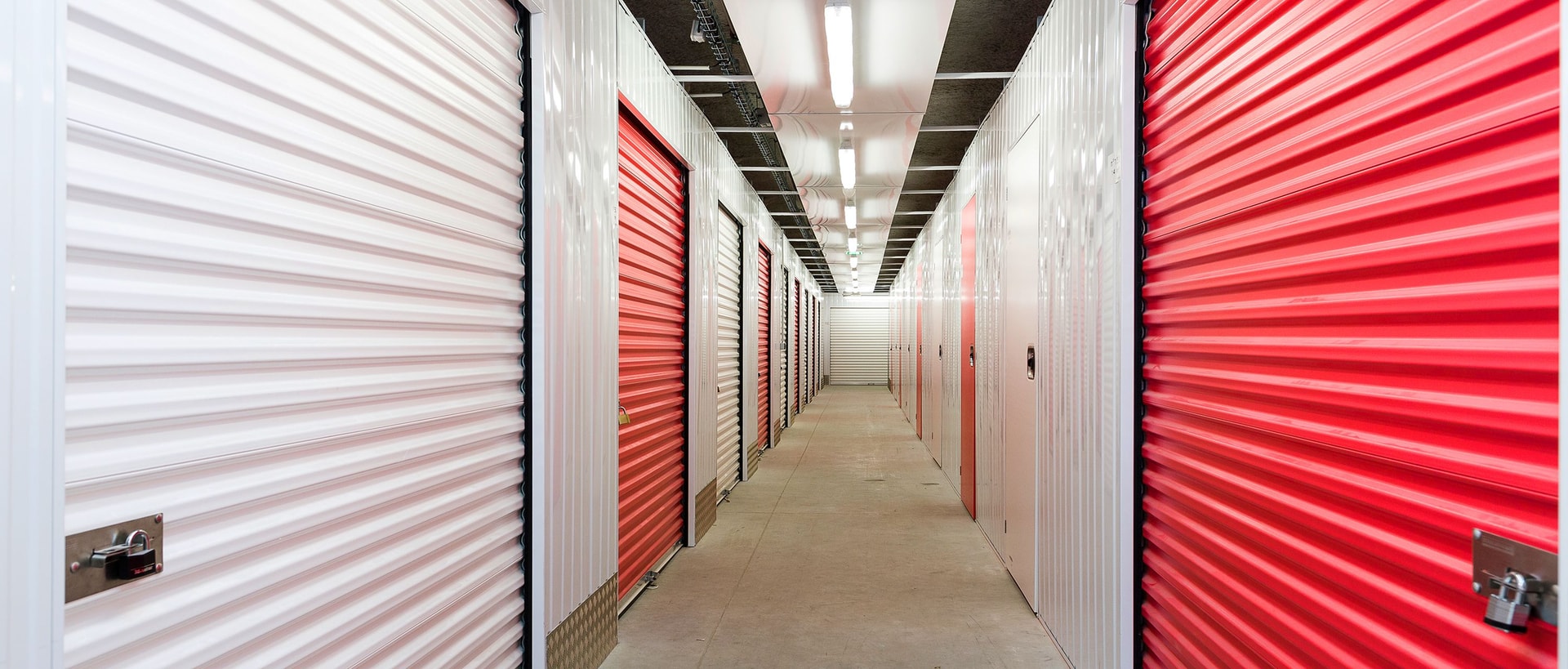 Indoor corridor lined with white and red roller shutter storage units at HOMEBOX La Rochelle