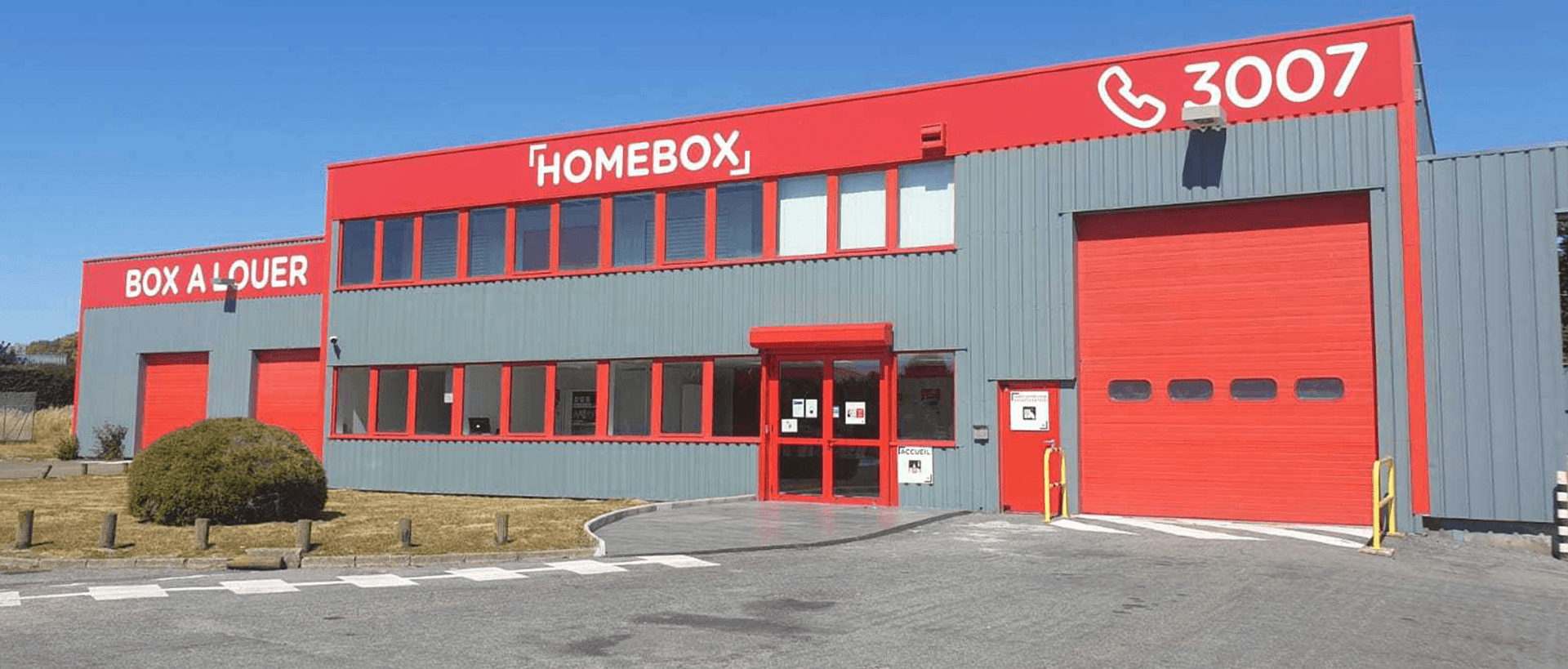 Red and grey two-storey facade with HOMEBOX sign and loading bay doors under blue sky at HOMEBOX Maurepas, 7 rue Claude Bernard, Maurepas