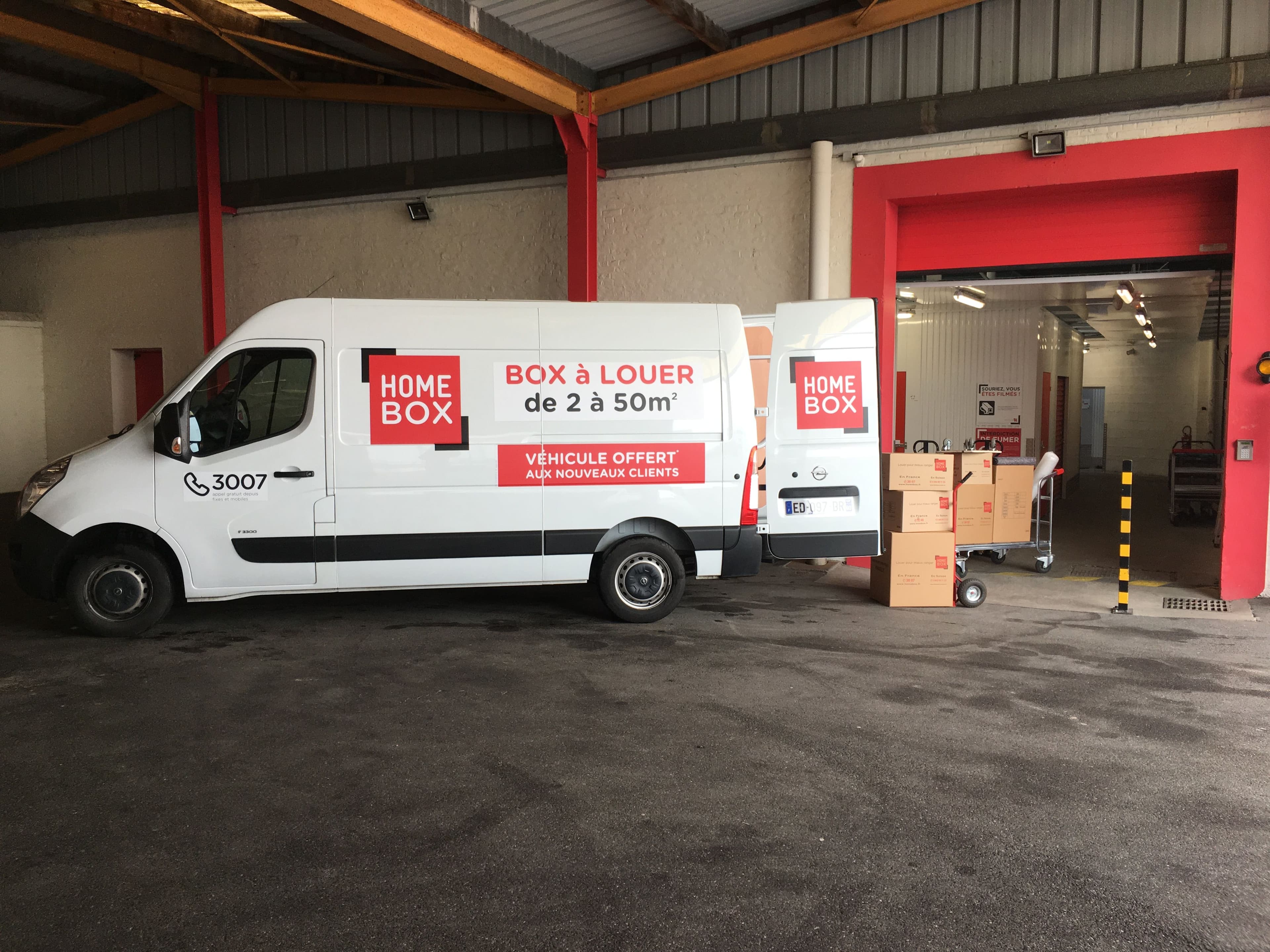Camionnette HOMEBOX Amiens stationnée devant une porte d’accès avec cartons de déménagement.