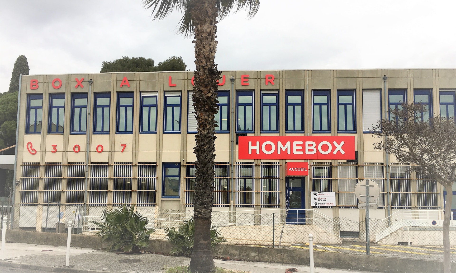 Beige building facade with Box à Louer lettering, HOMEBOX sign and palm tree in front at HOMEBOX Toulon - Les Routes, 264 Avenue André le Chatelier, Toulon