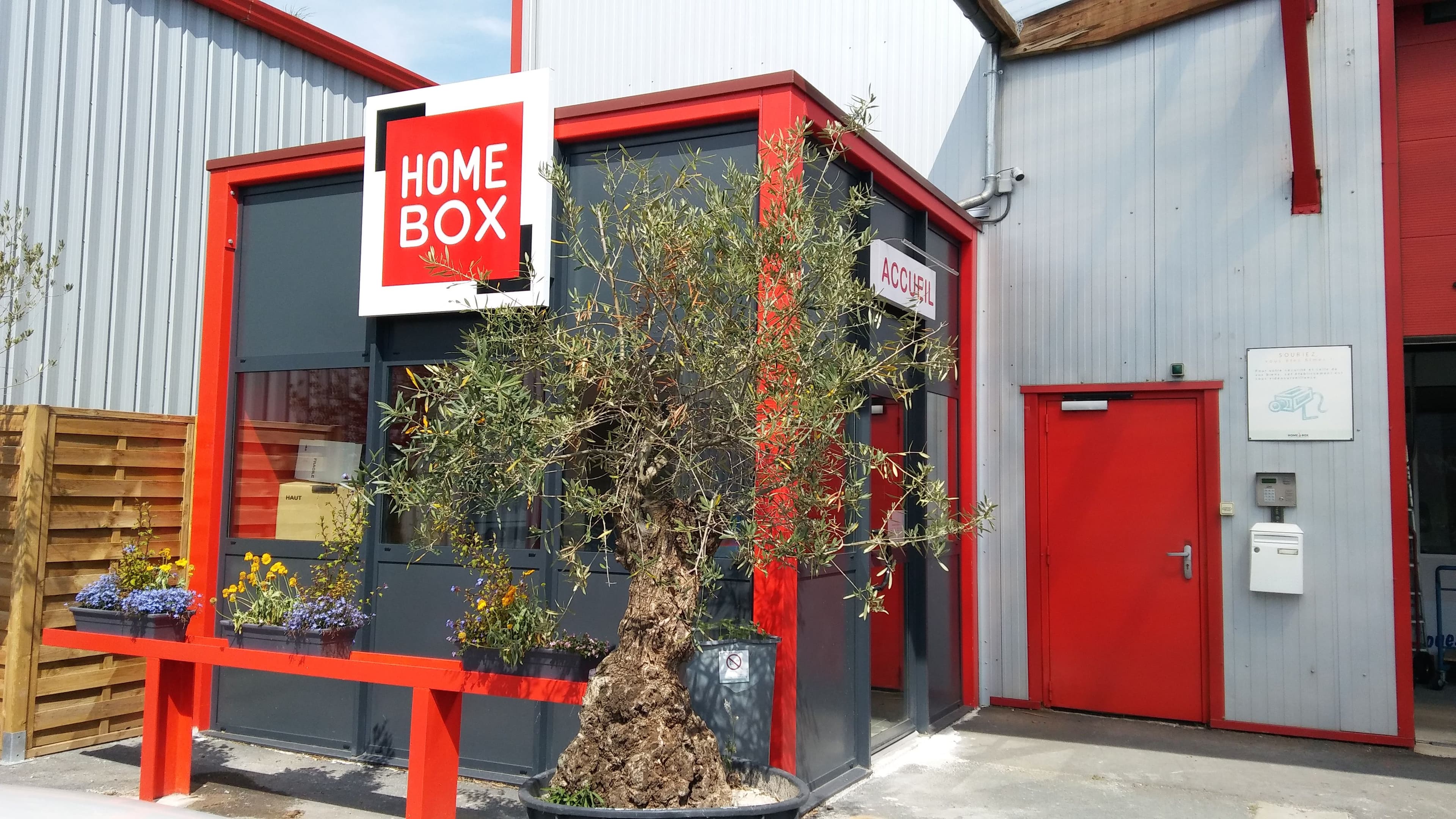 Entrée accueil du centre HOMEBOX Caen Ouest avec enseigne rouge et blanche.