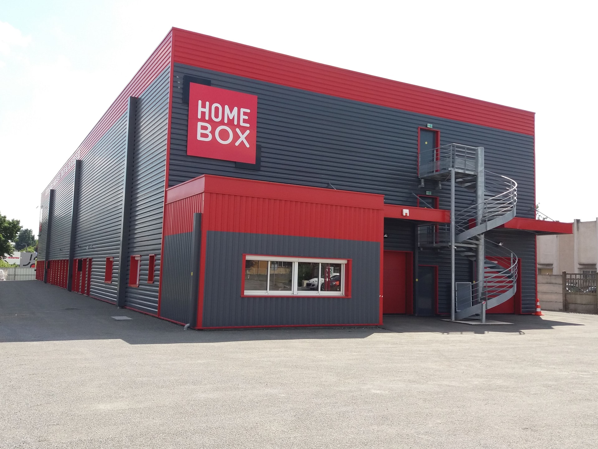 Red and grey corrugated facade with spiral staircase and HOMEBOX logo at HOMEBOX Angoulême, 3 chemin de Chaumontet, Gond Pontouvre