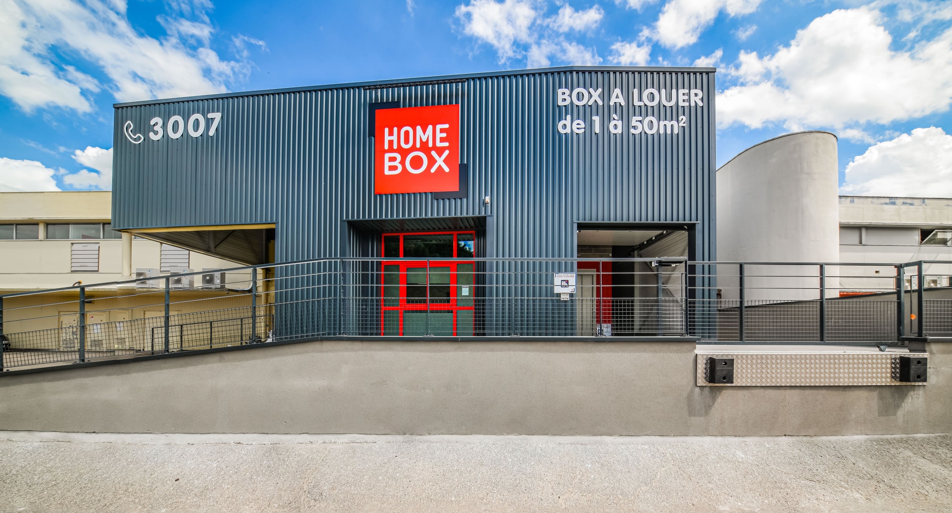 Grey warehouse with red logo, Box à louer signage and fenced entrance at HOMEBOX Thionville, 17 boucle du Ferronnier, Thionville