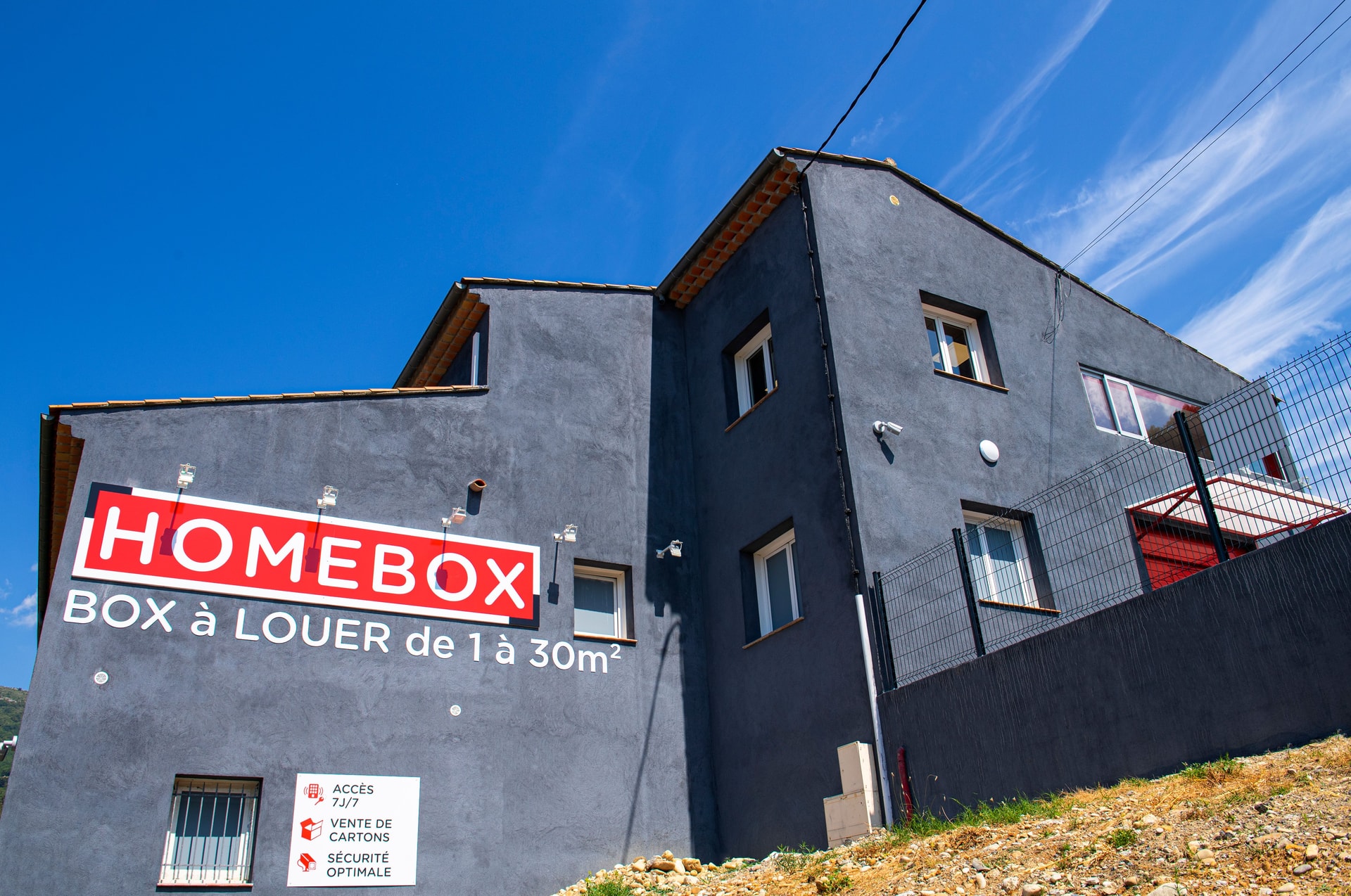 Façade grise avec grande enseigne HOMEBOX Box à Louer sous ciel bleu, HOMEBOX Nice-Carros, 650 route de la Baronne à Gattières