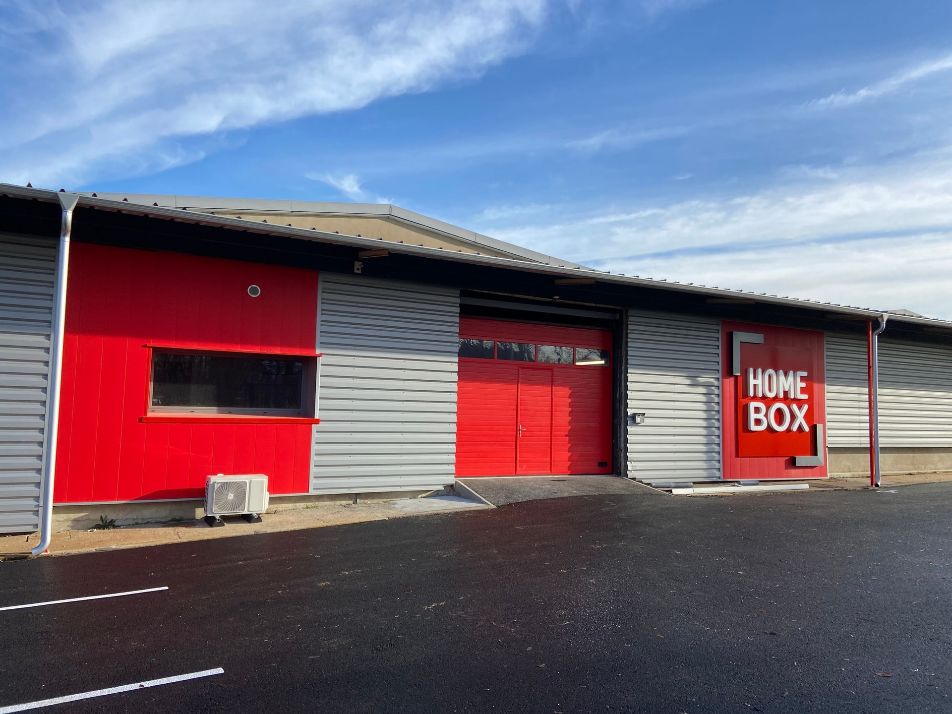 Grey and red metal warehouse facade with HOMEBOX sign and red garage doors at HOMEBOX Bourges, Allée Napoléon III, Bourges