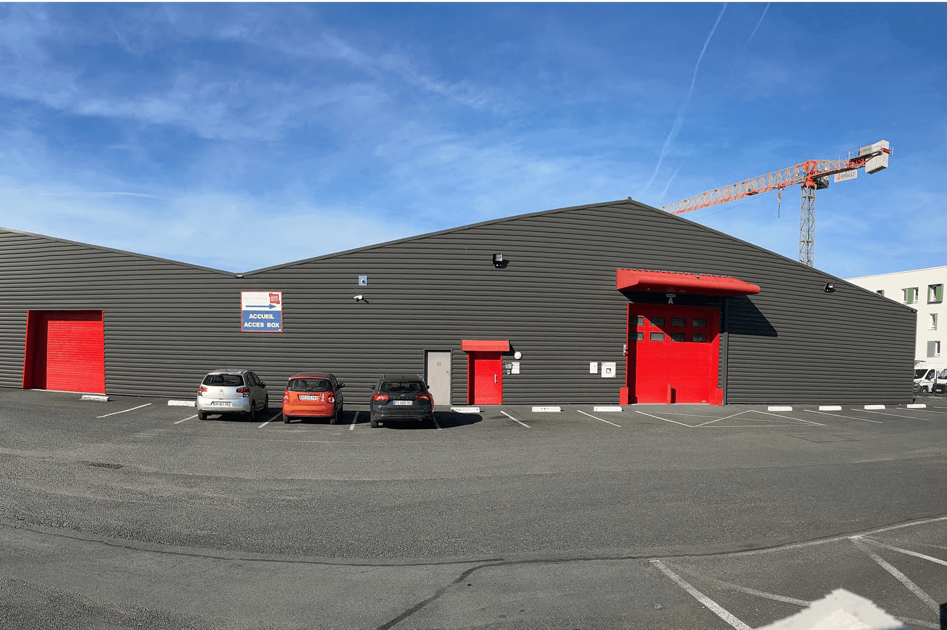 Façade noire avec portes de quai rouges et parking devant le bâtiment, HOMEBOX Tours, 9 rue Joseph Cugnot à Joué-les-Tours