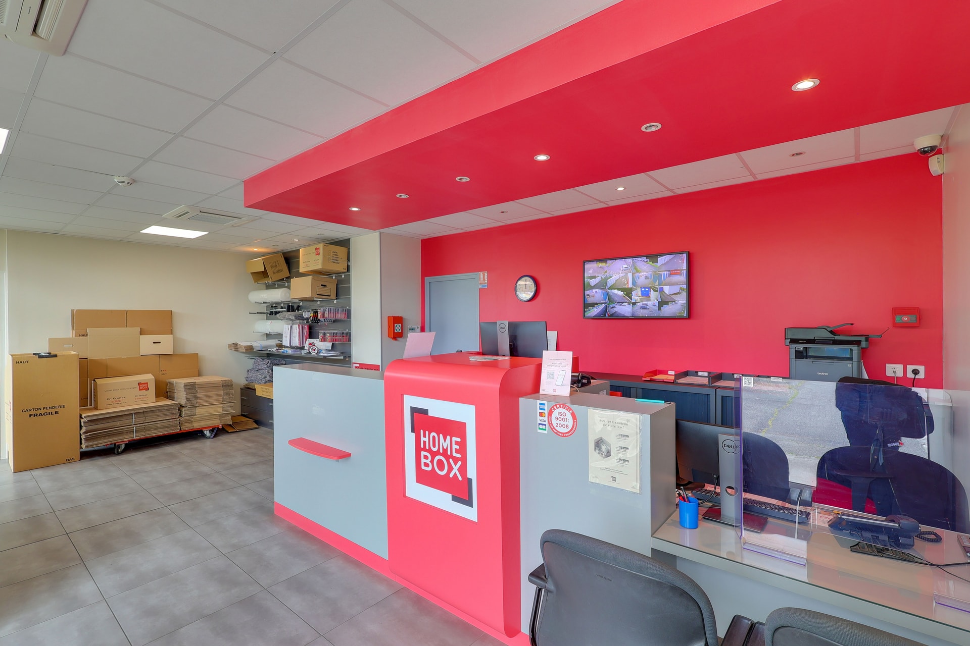 Comptoir d'accueil rouge avec écran de vidéosurveillance et postes de travail du centre HOMEBOX Toulouse Babinet