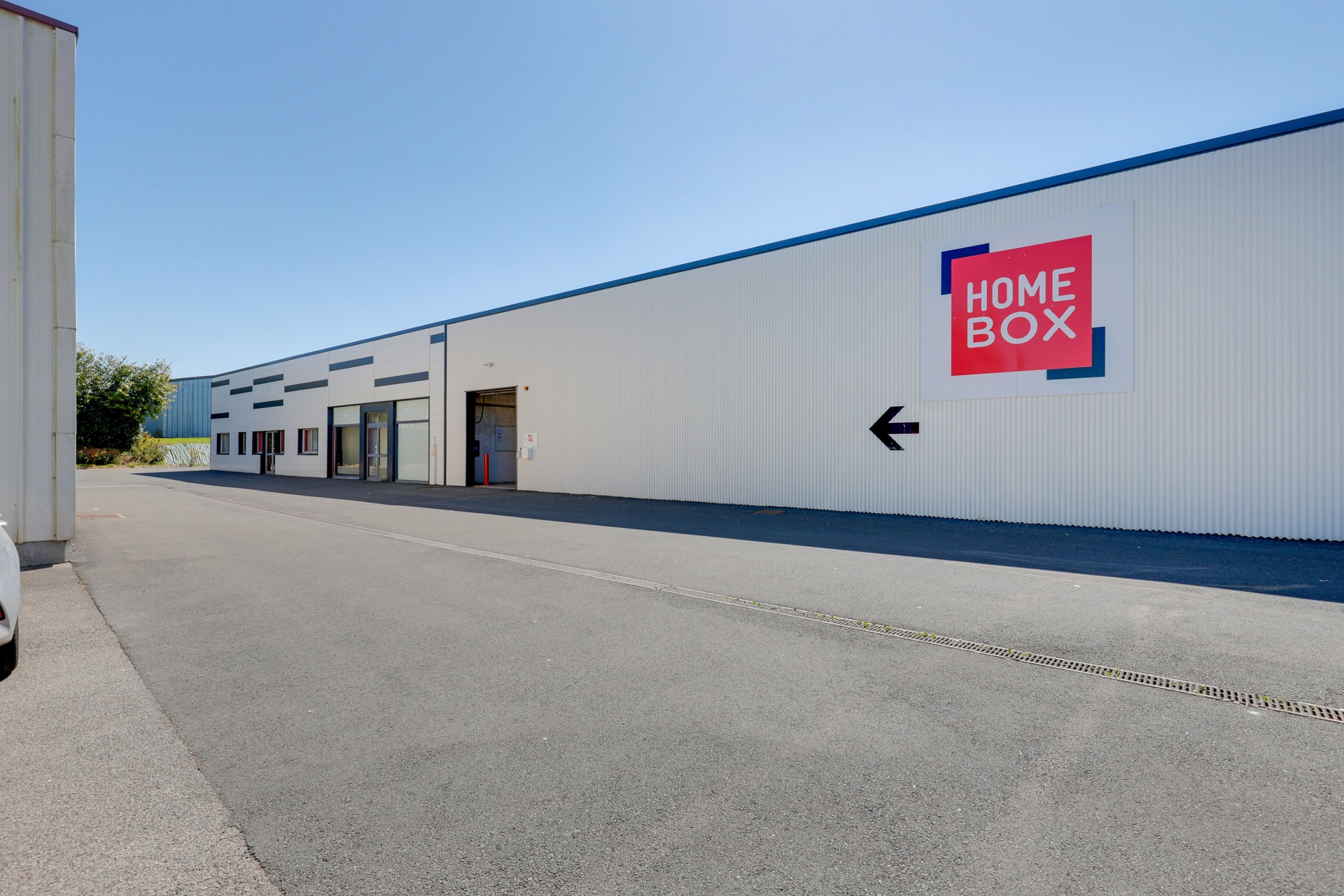 Façade blanche du bâtiment industriel avec enseigne directionnelle, HOMEBOX Quimper Nord, 19 rue Nobel - Bât. 21 à Quimper