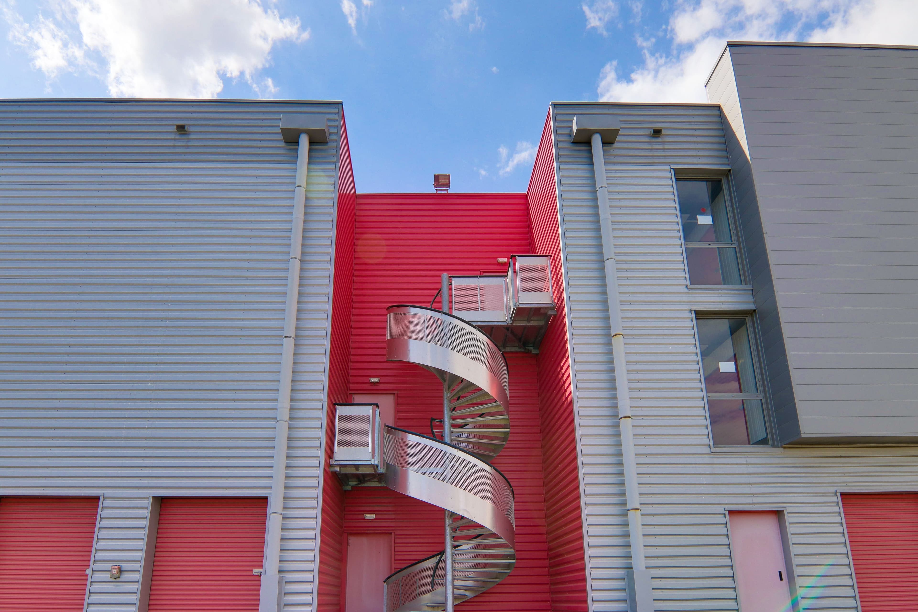 Escalier extérieur en colimaçon du centre HOMEBOX Avignon sur fond rouge et gris.
