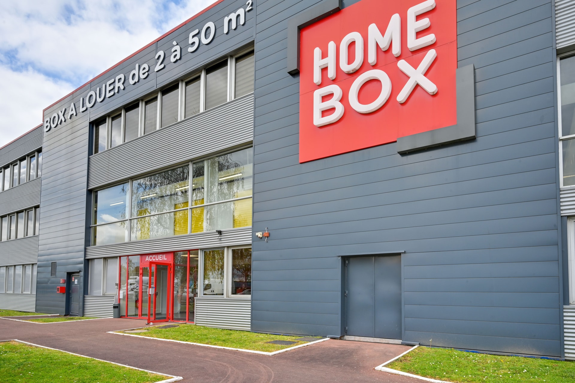 Façade grise avec enseigne HOMEBOX rouge et accueil rouge, HOMEBOX Plaisir, 15 rue Descartes à Plaisir
