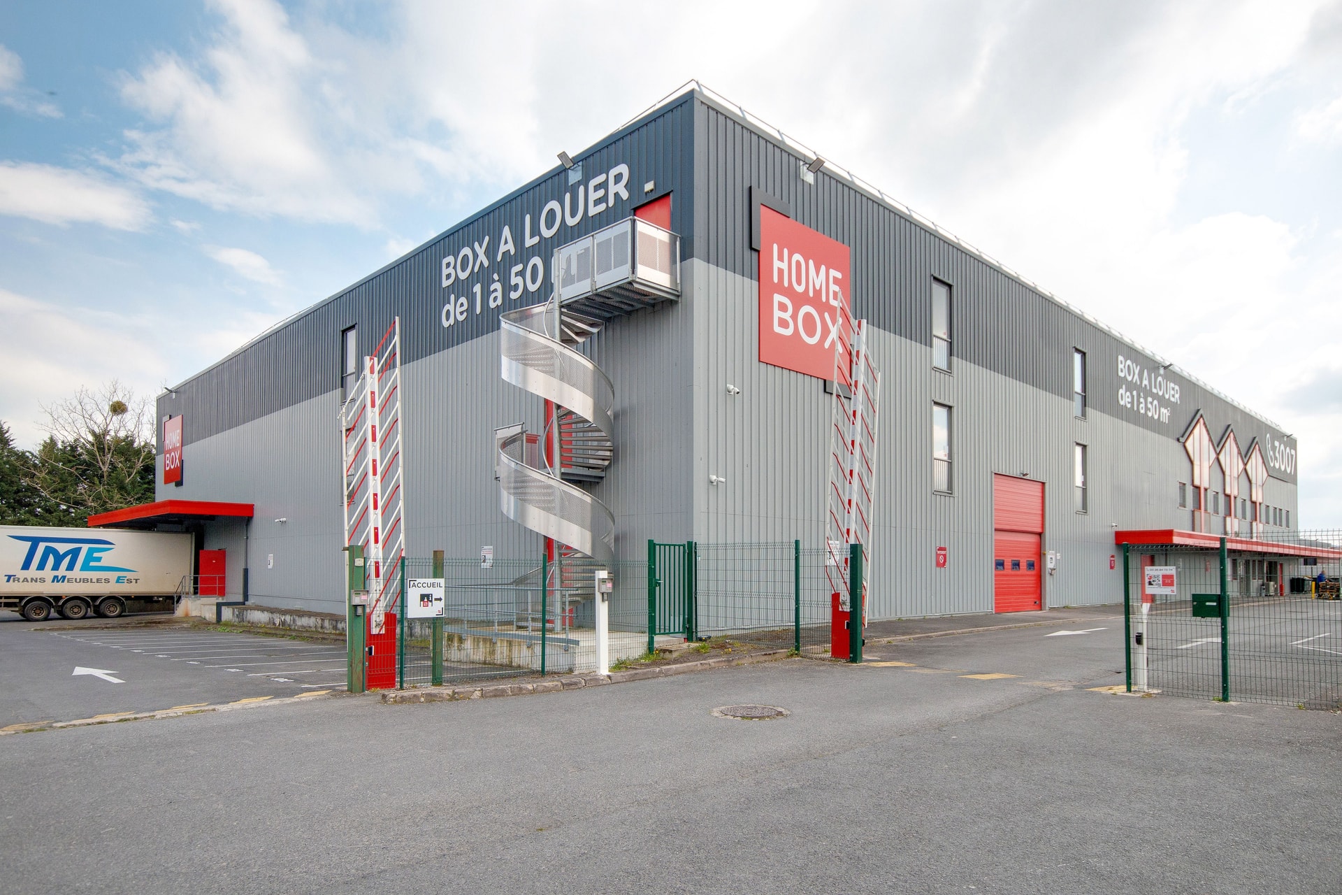 Façade grise du bâtiment avec enseigne HOMEBOX et escalier hélicoïdal extérieur, HOMEBOX Reims Sud, Rue William Shakespeare à Reims
