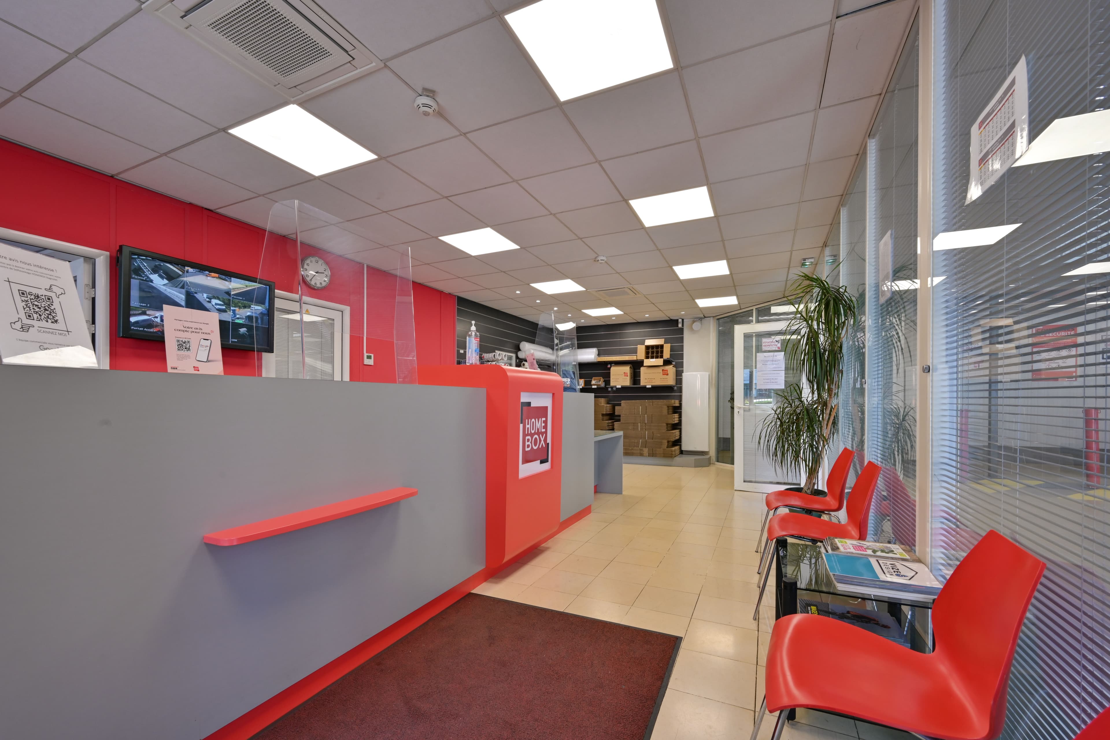 Comptoir d’accueil du centre HOMEBOX Bagnolet avec sièges pour clients et mur rouge.