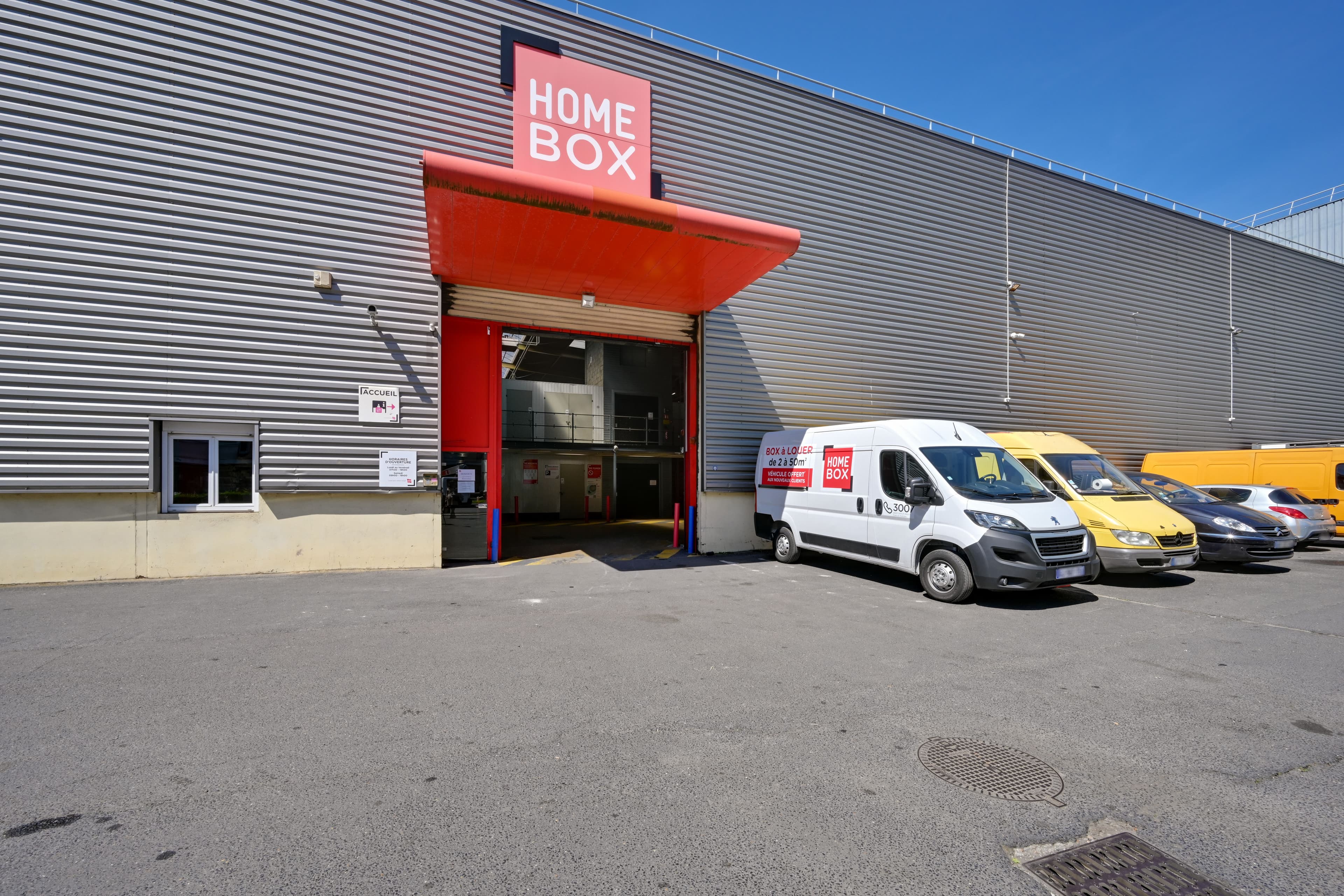 Entrée couverte du centre HOMEBOX Bagnolet avec utilitaires stationnés à proximité.