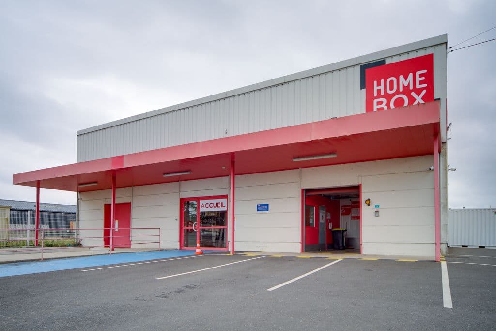 Entrée du centre HOMEBOX Blois avec façade blanche et rouge et accès au parking.