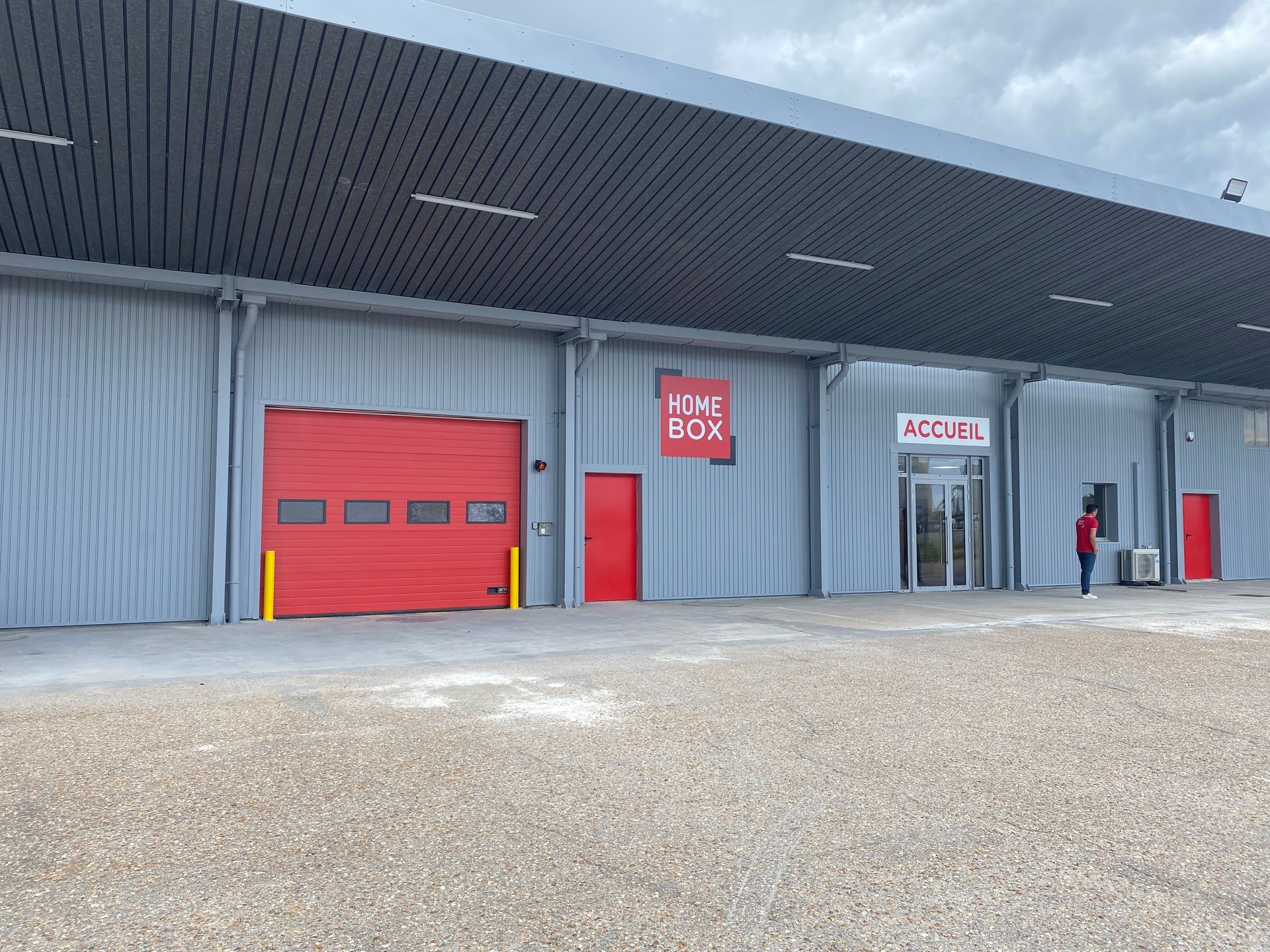 Grey warehouse facade with red loading door and reception entrance at HOMEBOX Orléans Nord, 165 Impasse des Moulins, Saran