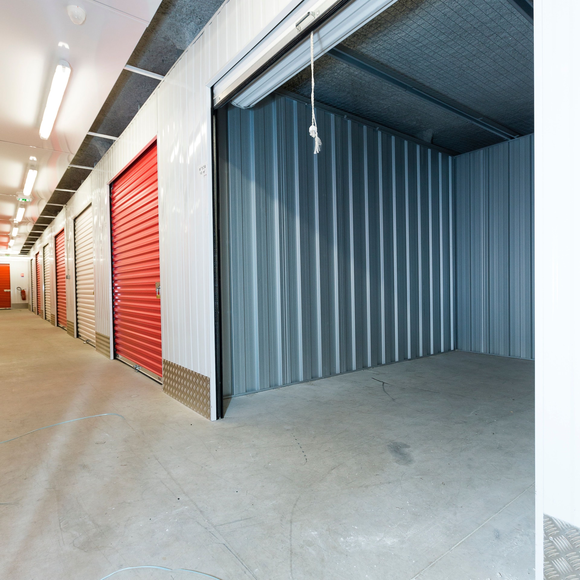 Couloir éclairé avec portes de box rouges et box ouvert sur cloisons métalliques du centre HOMEBOX Madrid Móstoles