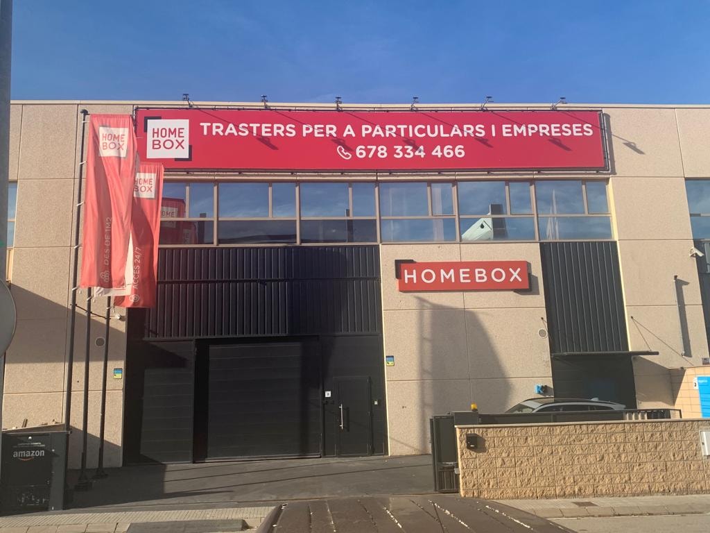 Industrial building facade with red HOMEBOX signage and flags at HOMEBOX Cerdanyola, Carrer de l'Or, 8, Cerdanyola del Vallès