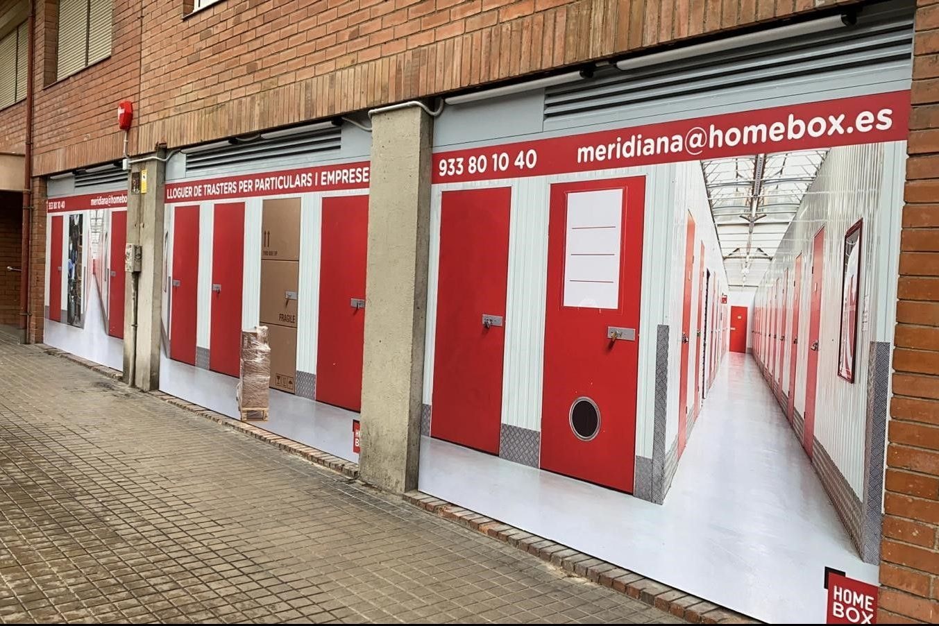 Façade en briques avec visuel publicitaire de box rouges et coordonnées, HOMEBOX Barcelona Meridiana, Carrer Campeny 30 0 Barcelona Barcelona à Barcelona