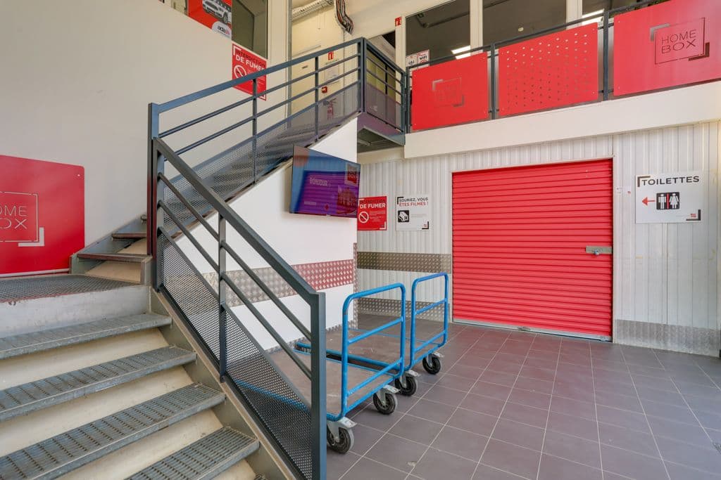 Espace intérieur avec escalier, chariots et portes roulantes rouges au centre HOMEBOX Cannes Mougins.