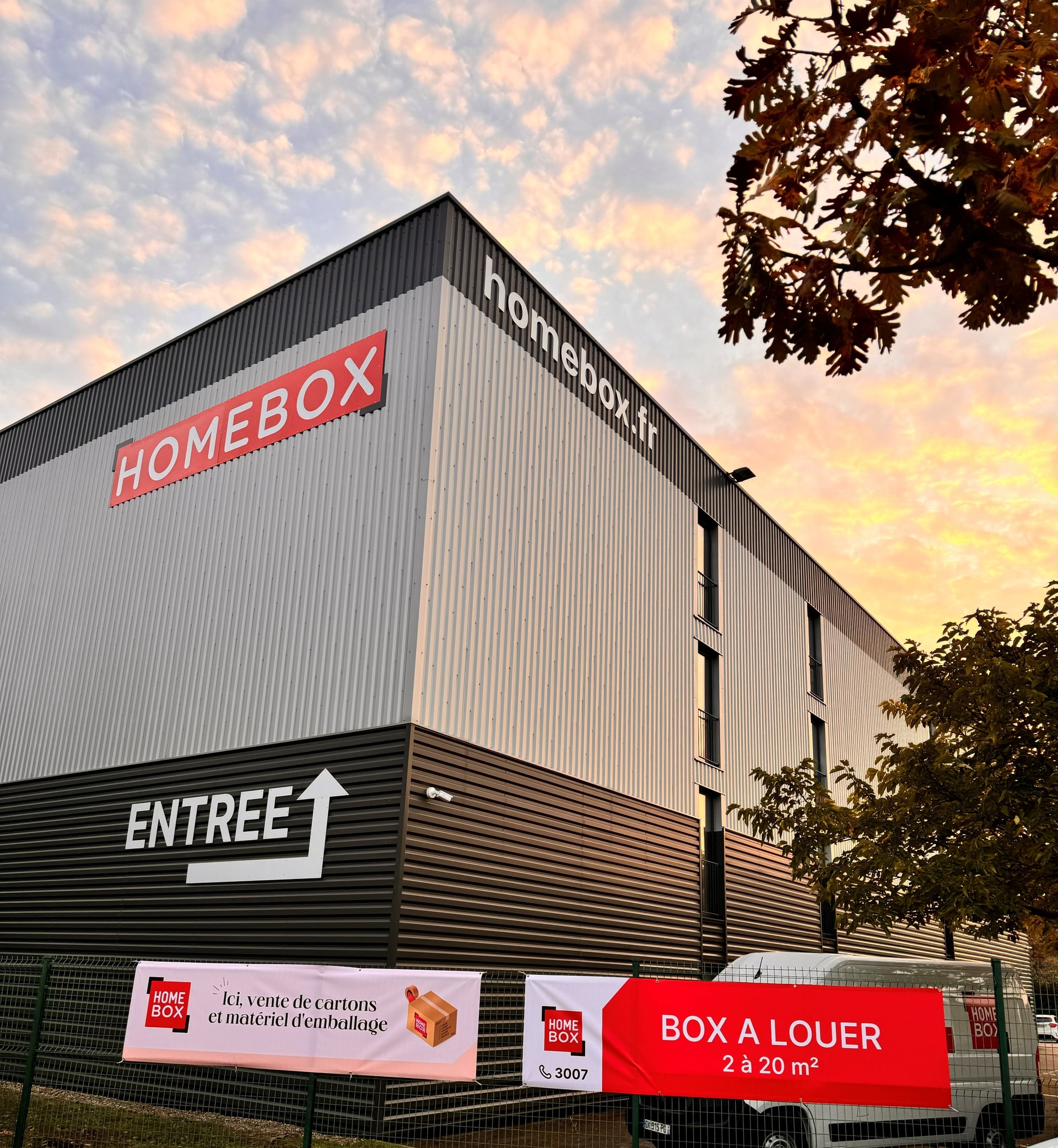 Self-storage warehouse facade with HOMEBOX logo and entrance sign at sunset at HOMEBOX Lyon Craponne, 225 avenue Pierre Auguste Roiret, Craponne