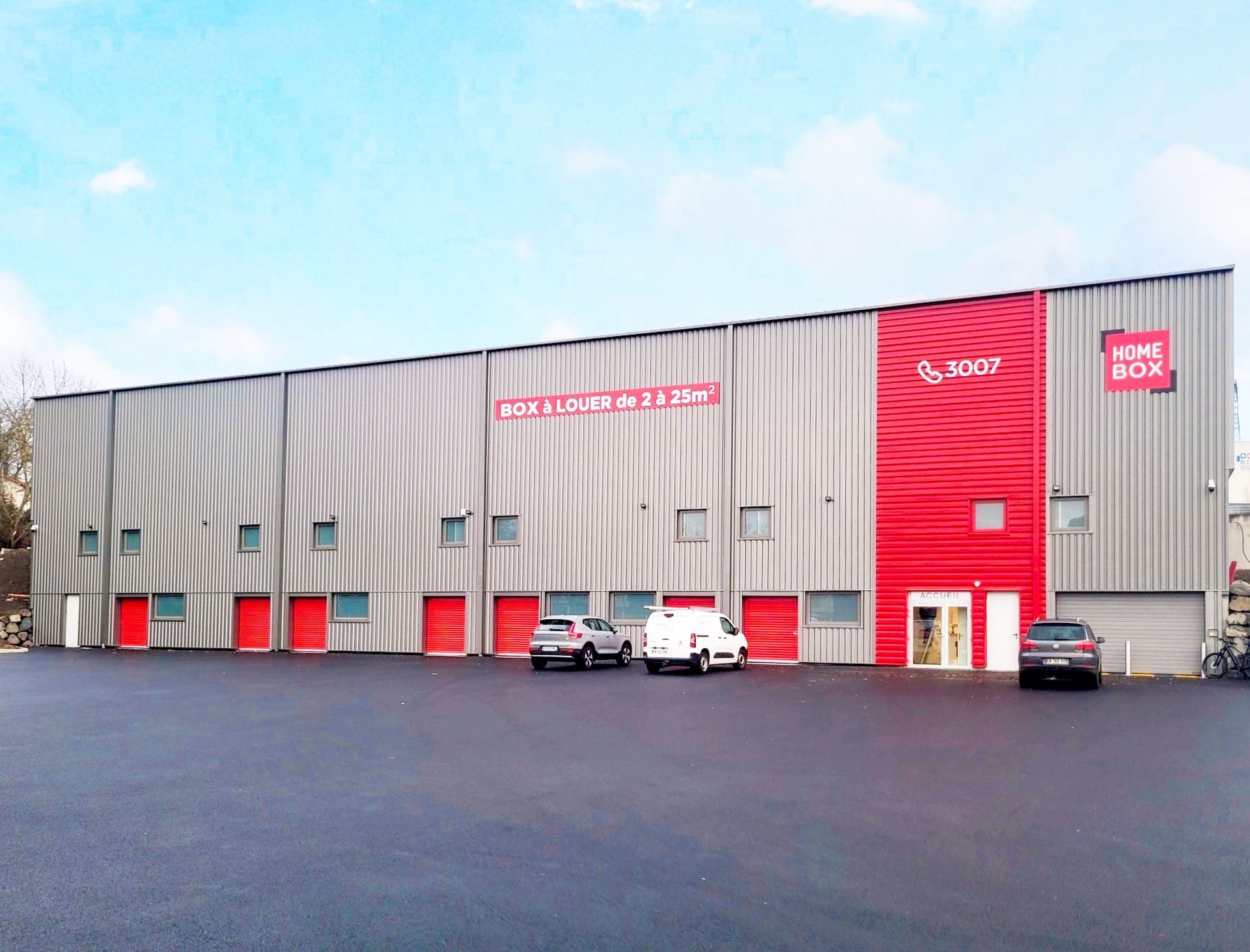 Long grey and red warehouse facade with Box à louer signage and parked cars at HOMEBOX Le Puy-en-Velay, 720 rue de Farnier corsac 2, Brives-Charensac