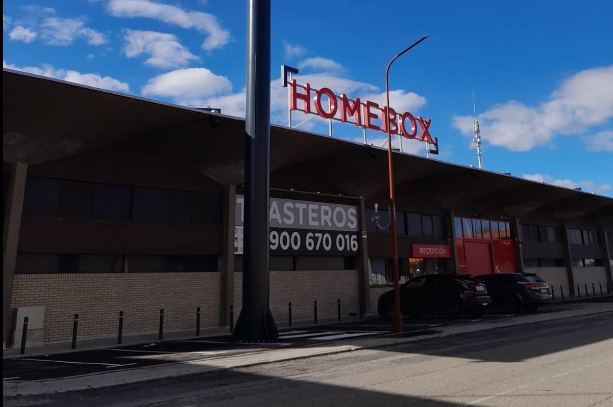 Building with illuminated rooftop sign and Trasteros panel above parking area at HOMEBOX Alcalá de Henares, N-II Ctra. Madrid-Barcelona Km 34, 200 Alcalá de Henares. Madrid, Alcalá de Henares