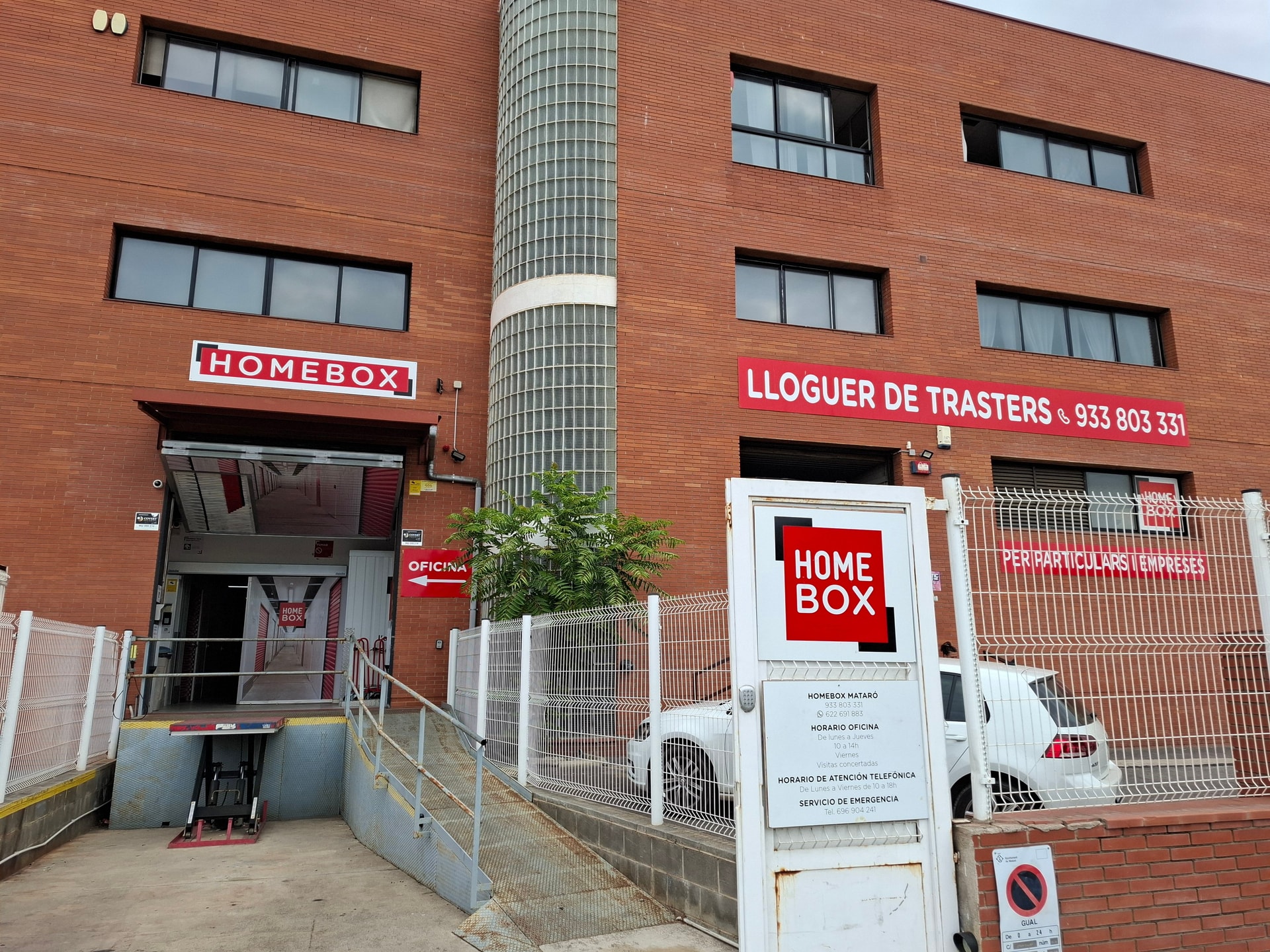 Red brick building with HOMEBOX sign, Lloguer de Trasters banner and ramp access at HOMEBOX Mataró, Carrer Josep Calvet 28, Mataró