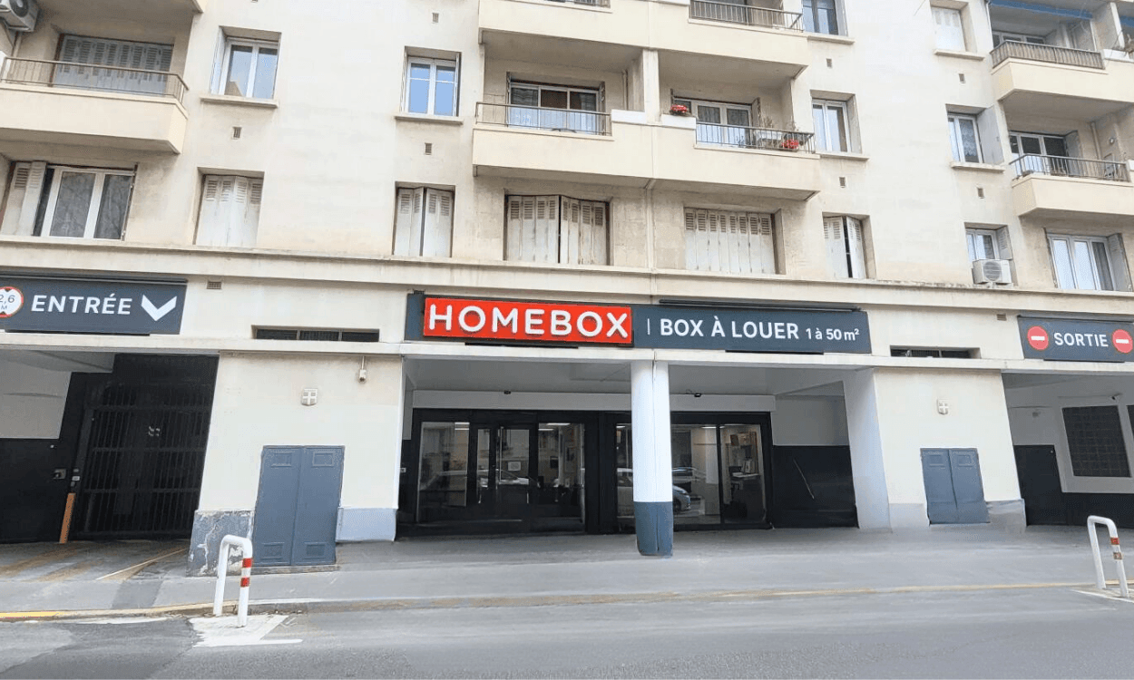 Storage center entrance under residential building with red HOMEBOX sign and entry-exit arrows at HOMEBOX Marseille - Le Rouet, 51 rue du Rouet, Marseille