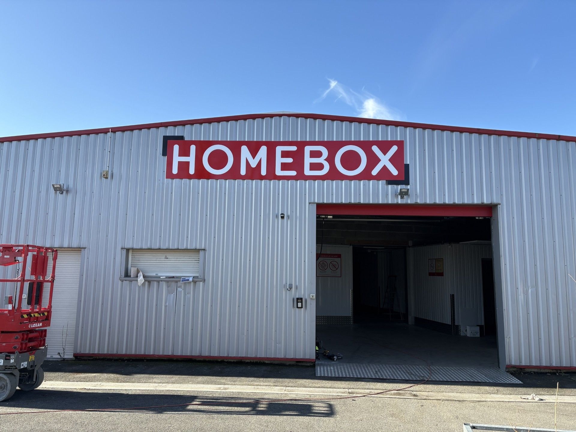 White and red warehouse facade with HOMEBOX sign and open hangar door at HOMEBOX Angoulême La Couronne, 17 rue de la Pinotière, La Couronne